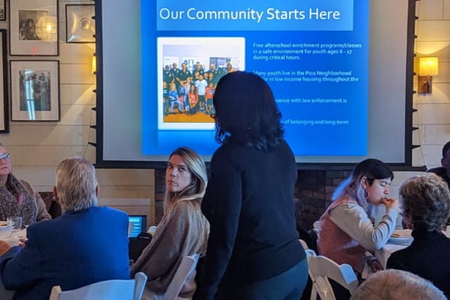 Presentation on community programs with diverse attendees seated, featuring a slide on youth enrichment and law enforcement collaboration.