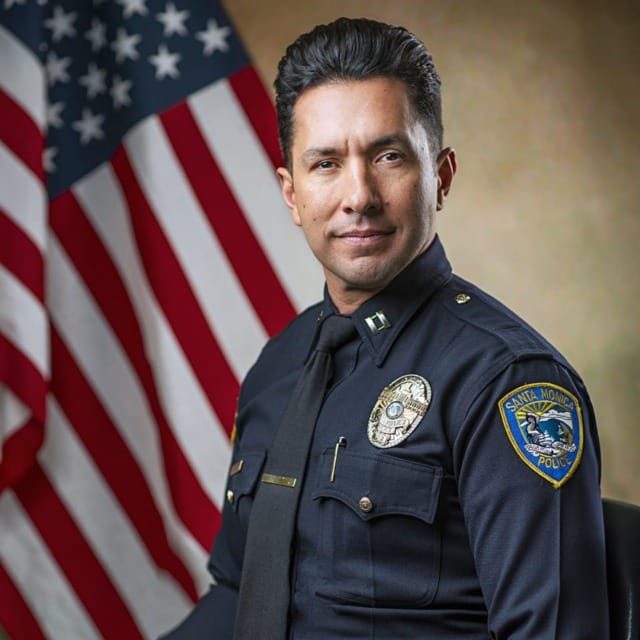 Police officer in uniform seated with an American flag in the background.