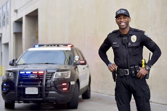 A smiling officer next to a police vehicle