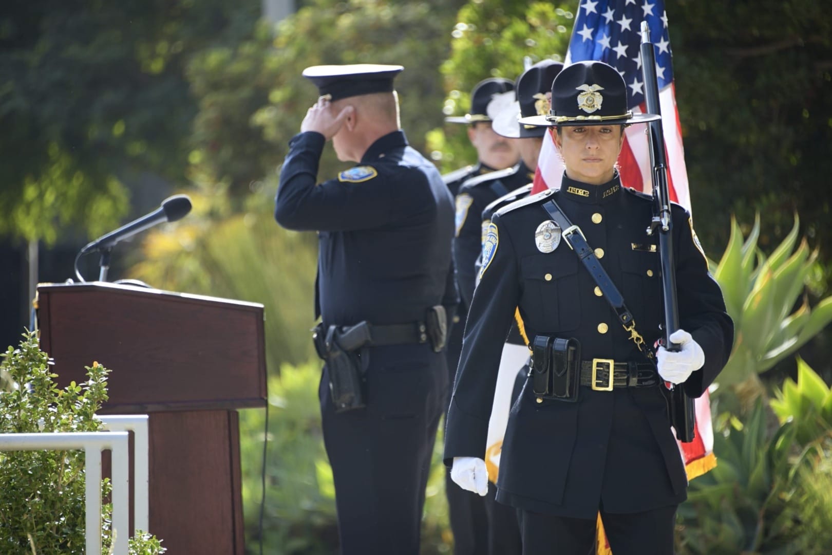 Police officer holding the American flag in a formal ceremony with colleagues standing nearby in uniform.