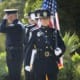 Police officer holding the American flag in a formal ceremony with colleagues standing nearby in uniform.