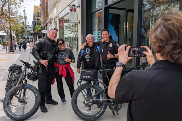 People posing with police officers on bicycles while another person takes a photo on a bustling city street.