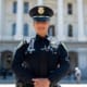 Police officer in uniform stands confidently in front of a large government building with columns.