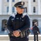 Police officer standing confidently in uniform in front of a large government building with a colleague in the background