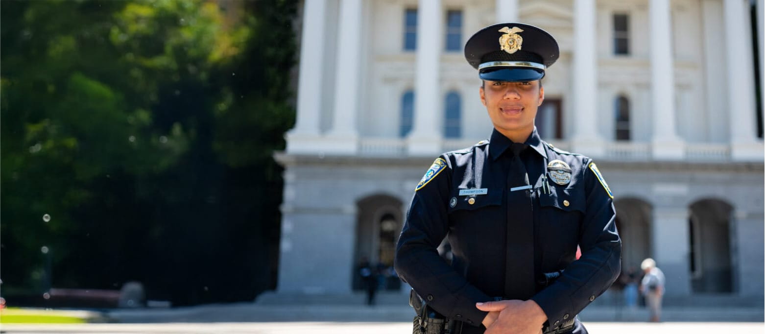 Police officer in uniform standing in front of a large government building with columns.