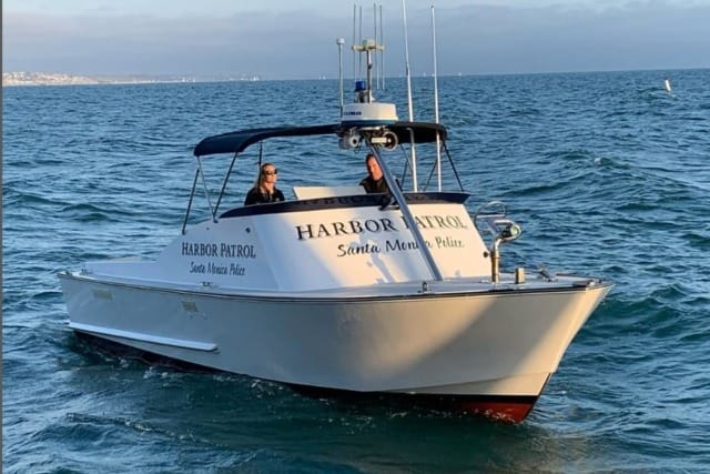 Harbor Patrol boat on the ocean with two people on board under a clear blue sky.