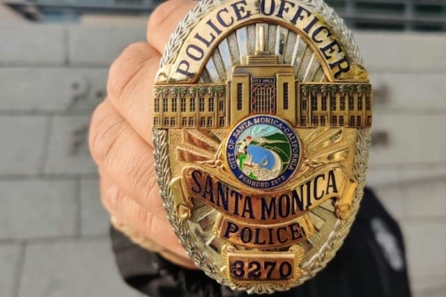 Police officer holding a gold Santa Monica badge with intricate design and city emblem in the center