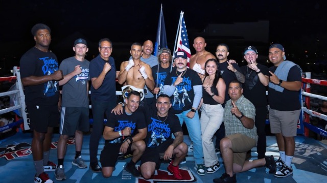 Group of people posing in a boxing ring, some holding flags, with a night sky backdrop.