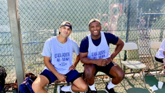 Two basketball players sitting on a bench wearing jerseys that read "Coach Jackson's All-Stars 2023" on a sunny day.