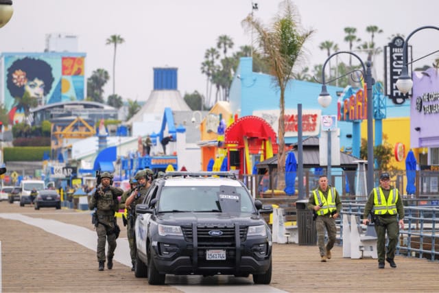 Police officers and security personnel patrolling a colorful outdoor amusement area with palm trees and murals in the background.