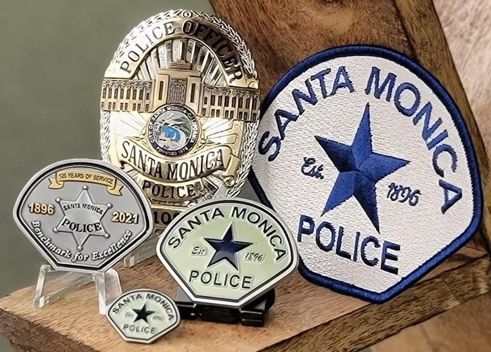 Santa Monica Police badges and patch displayed on a wooden surface representing years of service and standards for excellence.